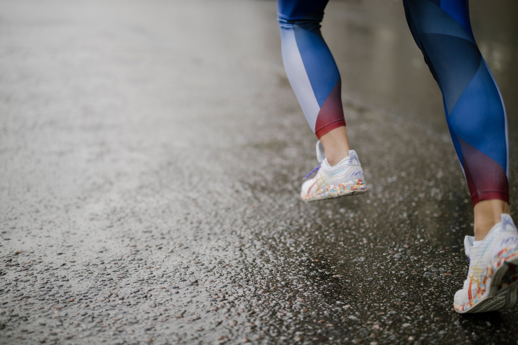 Runner's legs wearing shoes on wet pavement